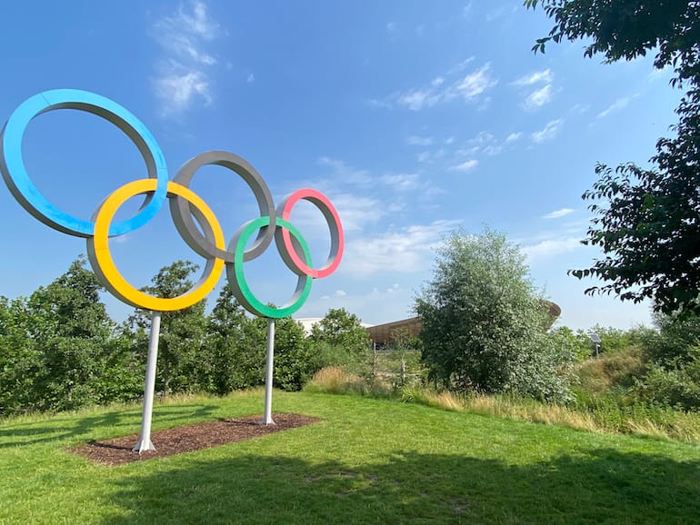 Olympic Rings with velodrome in distance at Queen Elizabeth Olympic Park East Bank London. Photo Credit: © Sarah Wood.